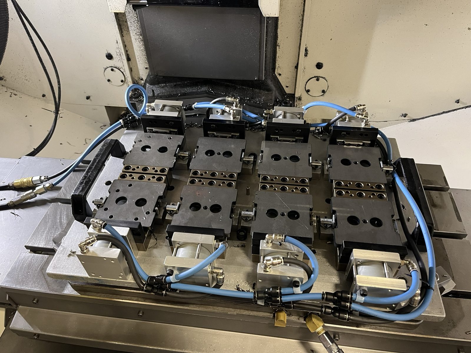 Eight-station pneumatic clamping fixture with blue air lines on a machine table